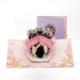 Birthday Bouquet 3D pop-up card front view: hands holding a wildflower bouquet, lilac cover behind, everpop