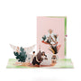 Bohemian Wedding 3D pop-up card front view: boho couple by a teepee on a meadow, pink cover behind, everpop