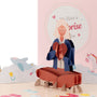 We Have a Surprise 3D pop-up card close-up: seated woman holding a paper heart among baby toys, everpop